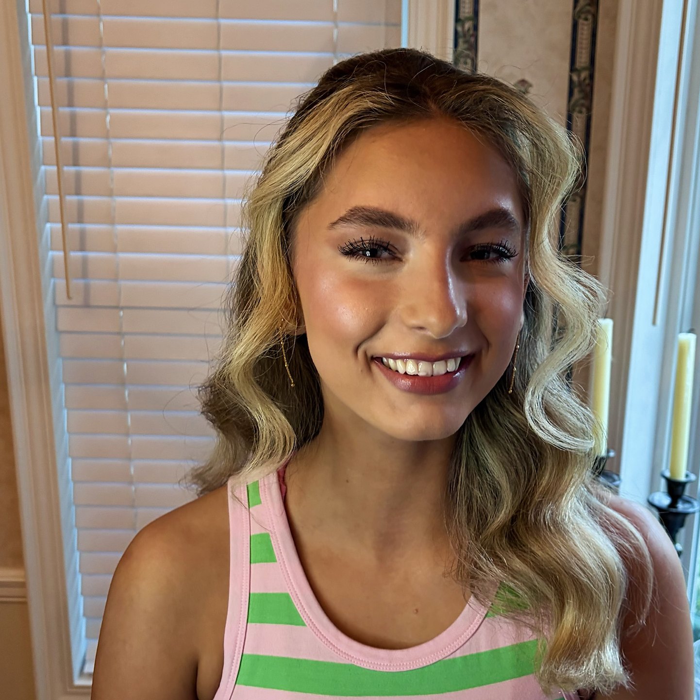 Smiling client with glowing skin, lashes and blonde waves pinned half up